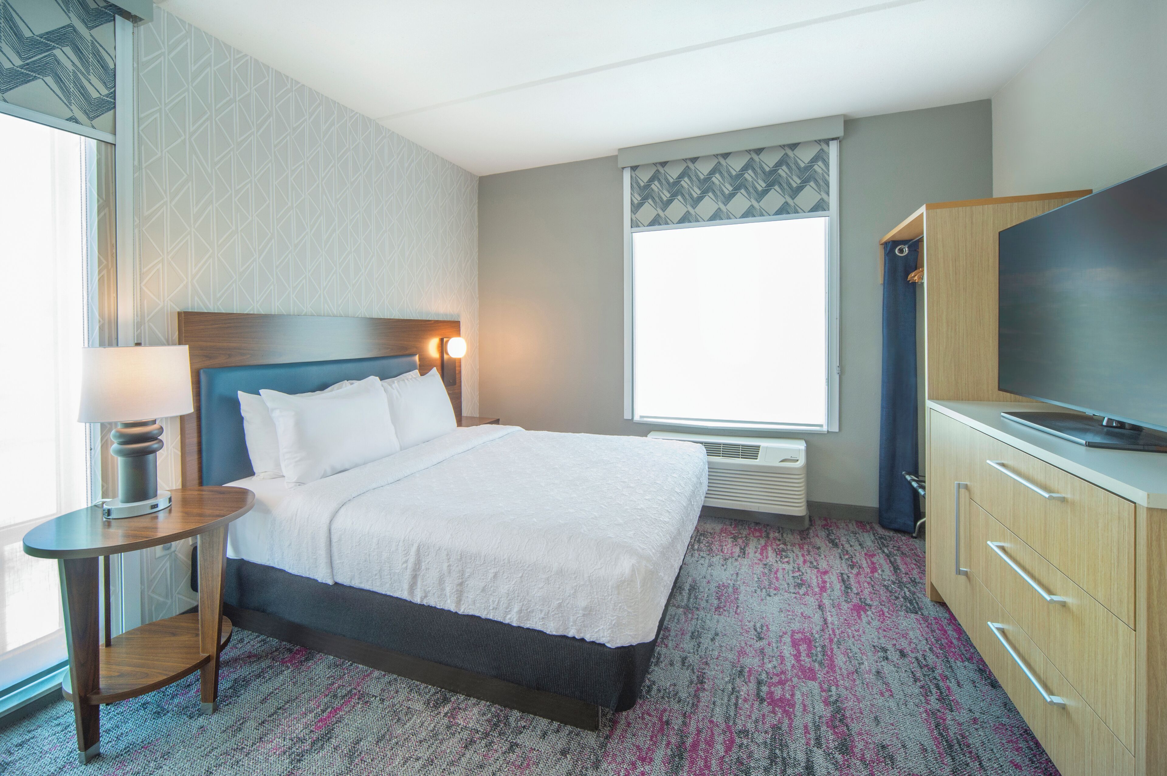 Une chambre d’hôtel avec un lit, une télévision, un bureau avec une lampe et une grande fenêtre.