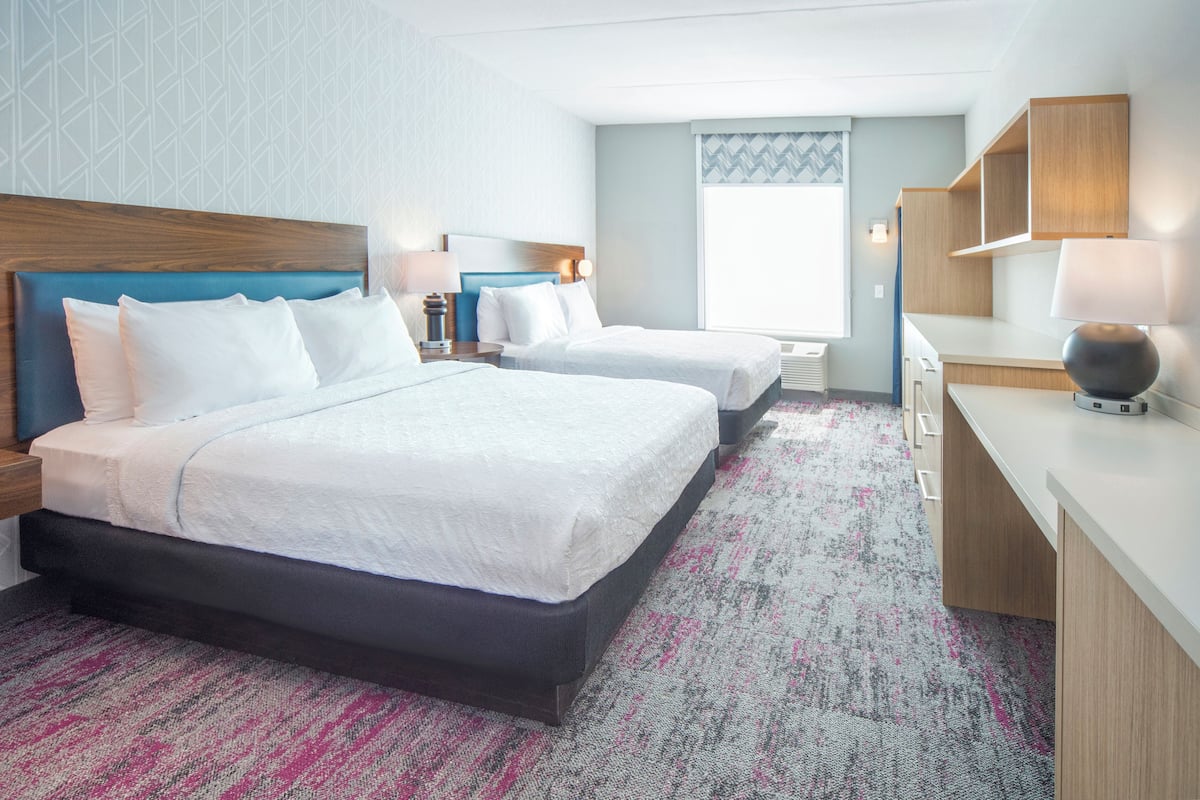 A hotel room with two beds, a desk, a chair, and a window with a view.