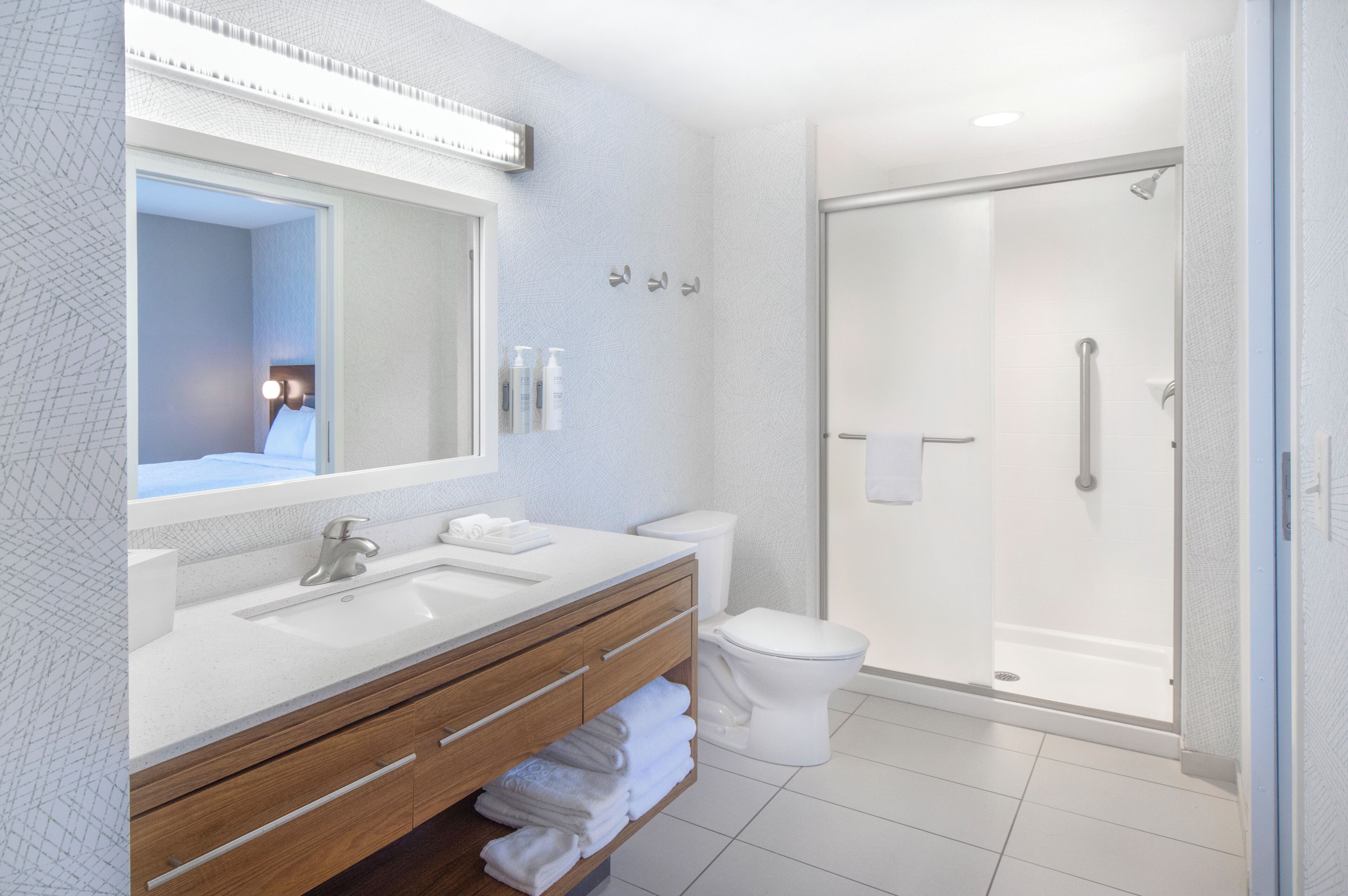Une salle de bain moderne avec un grand miroir, deux lavabos, des toilettes et une douche à parois de verre.