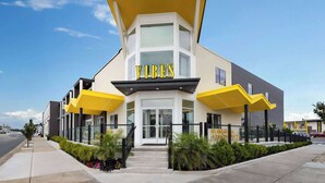 Un edificio moderno con un llamativo letrero que dice 'VIBES', que presenta un diseño arquitectónico único con un detalle amarillo en el techo y fachada de vidrio.