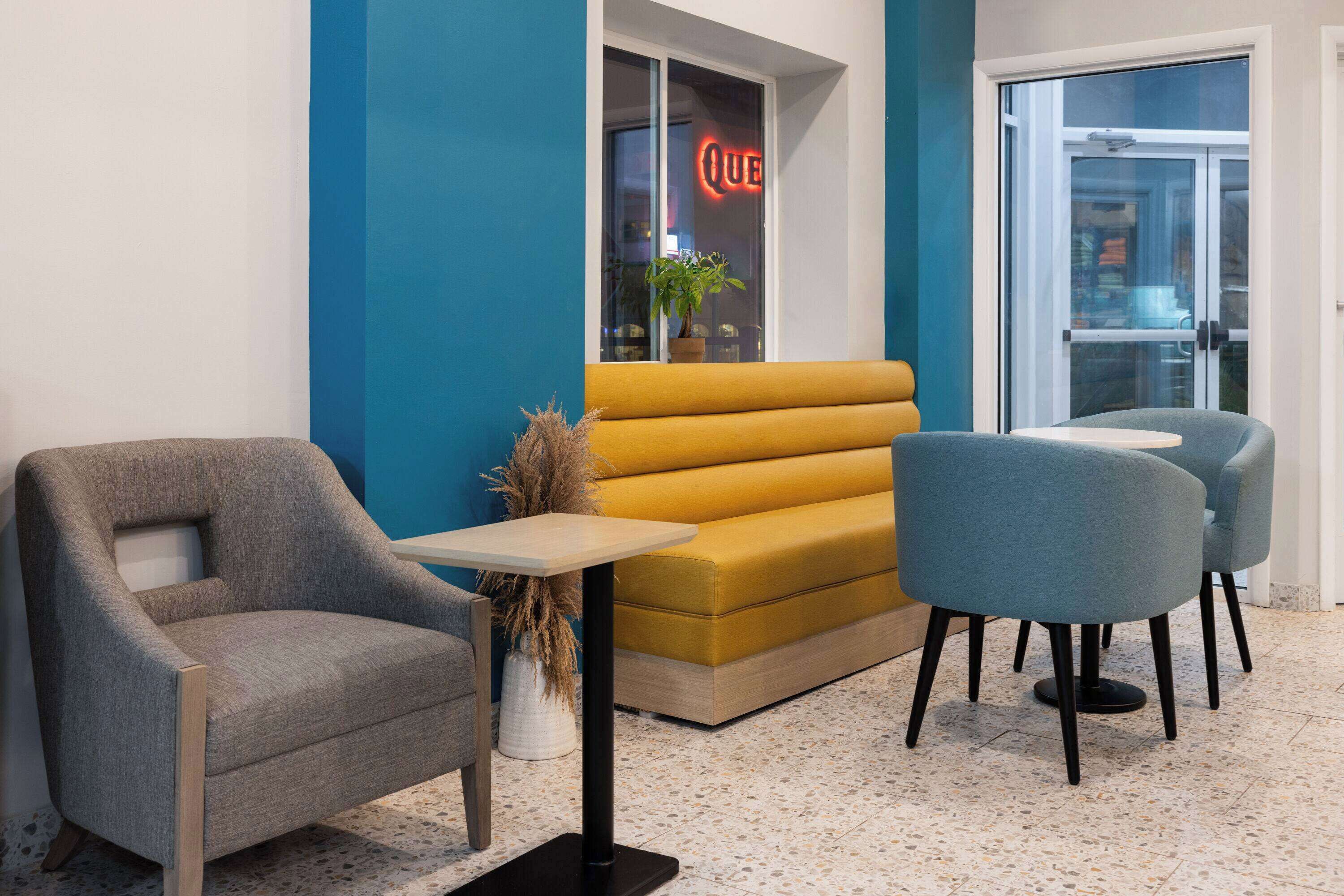 A modern waiting area with a yellow sofa, a grey armchair, and two blue chairs.