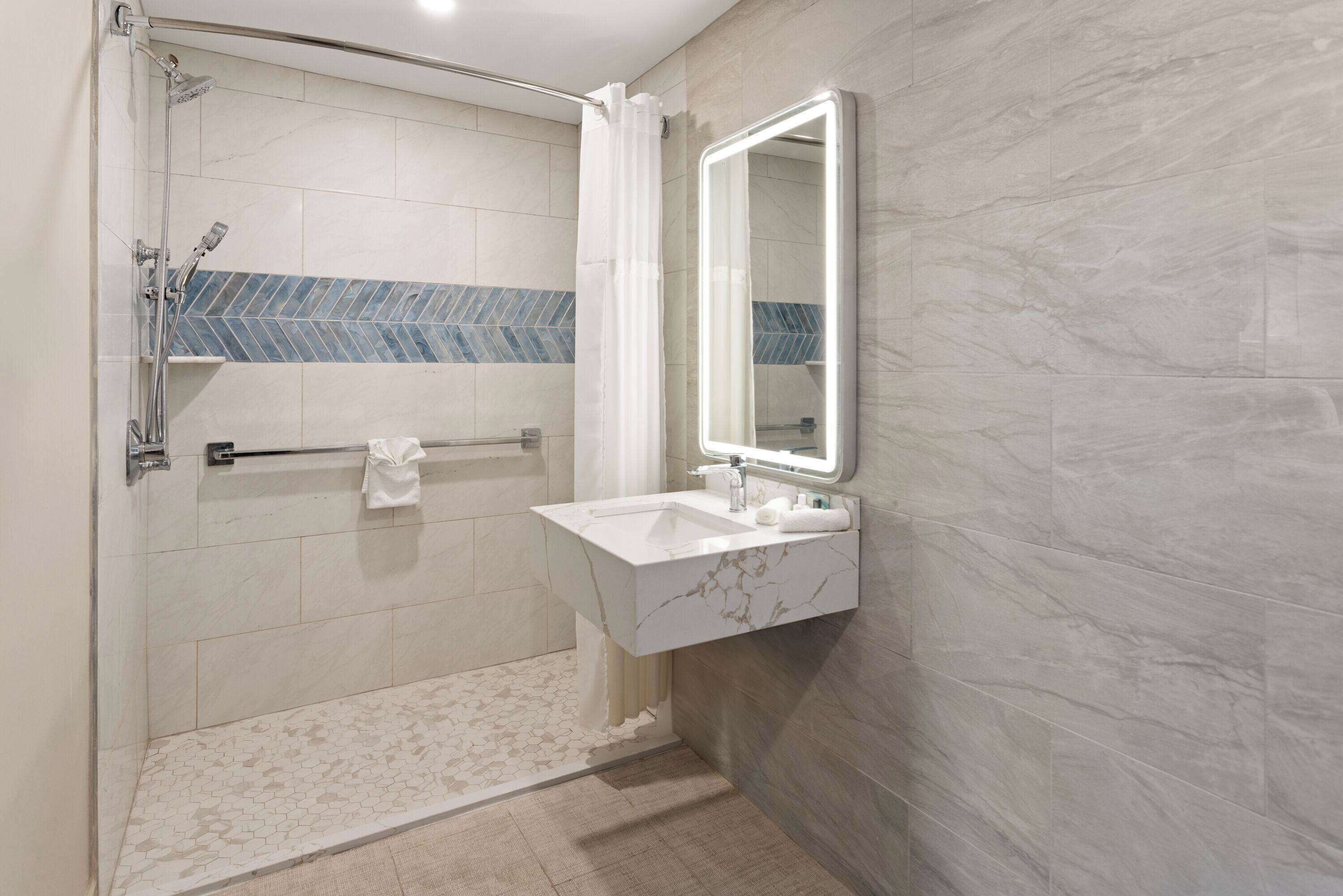 Un baño moderno con ducha de vidrio, lavamanos de mármol y un espejo grande.
