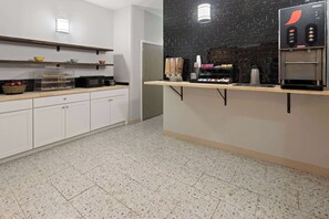 Una kitchenette equipada con microondas, cafetera y una cesta de fruta.
