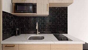 Una cocina moderna con un salpicadero de mármol negro, un lavamanos de acero inoxidable, un microondas integrado y armarios de madera.