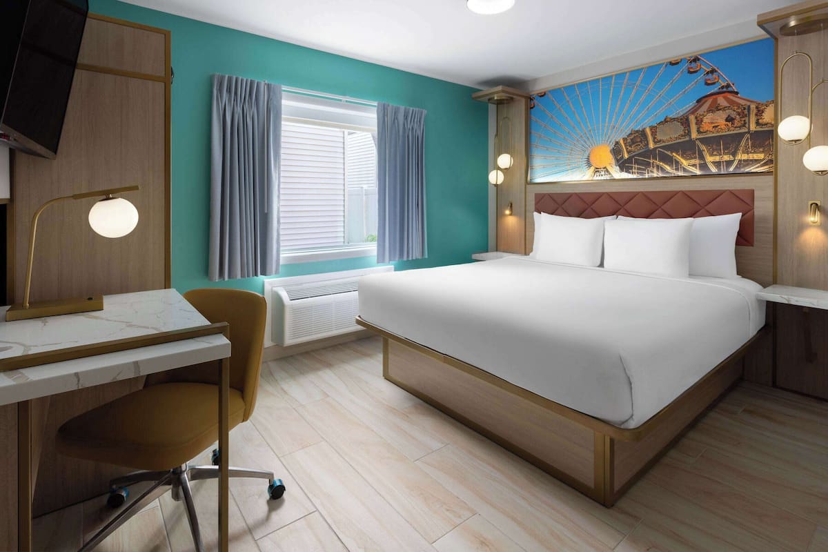 Habitación de hotel con cama, escritorio, silla y un amplio ventanal con cortinas.