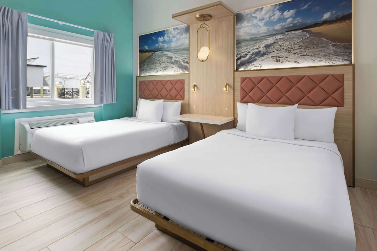 Habitación de hotel con dos camas, una ventana con cortinas, un calentador de pared y un cuadro de una playa.