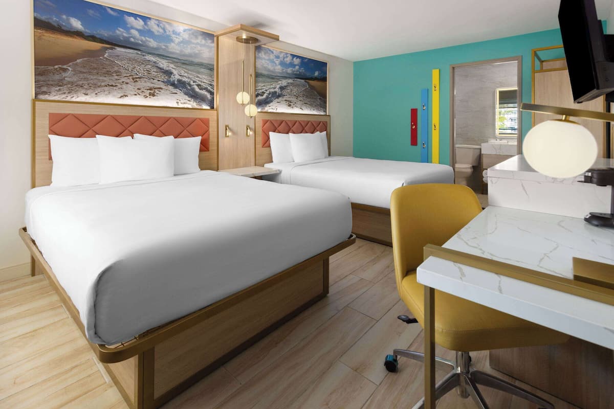 Habitación de hotel con dos camas, un escritorio con silla, televisor y baño visible a través de una puerta abierta.