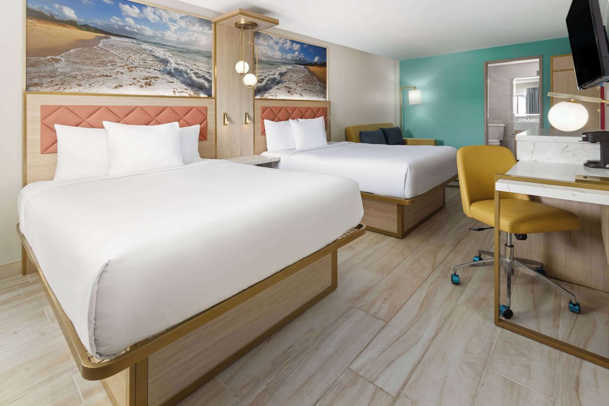 Habitación de hotel con dos camas, un escritorio con silla, televisión y un ventanal con vista a la playa.