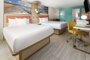 Habitación de hotel con dos camas, un escritorio con silla, televisión y un ventanal con vista a la playa.