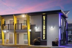 Un edificio moderno con un llamativo letrero que dice 'VIBES', varios balcones y un estacionamiento.