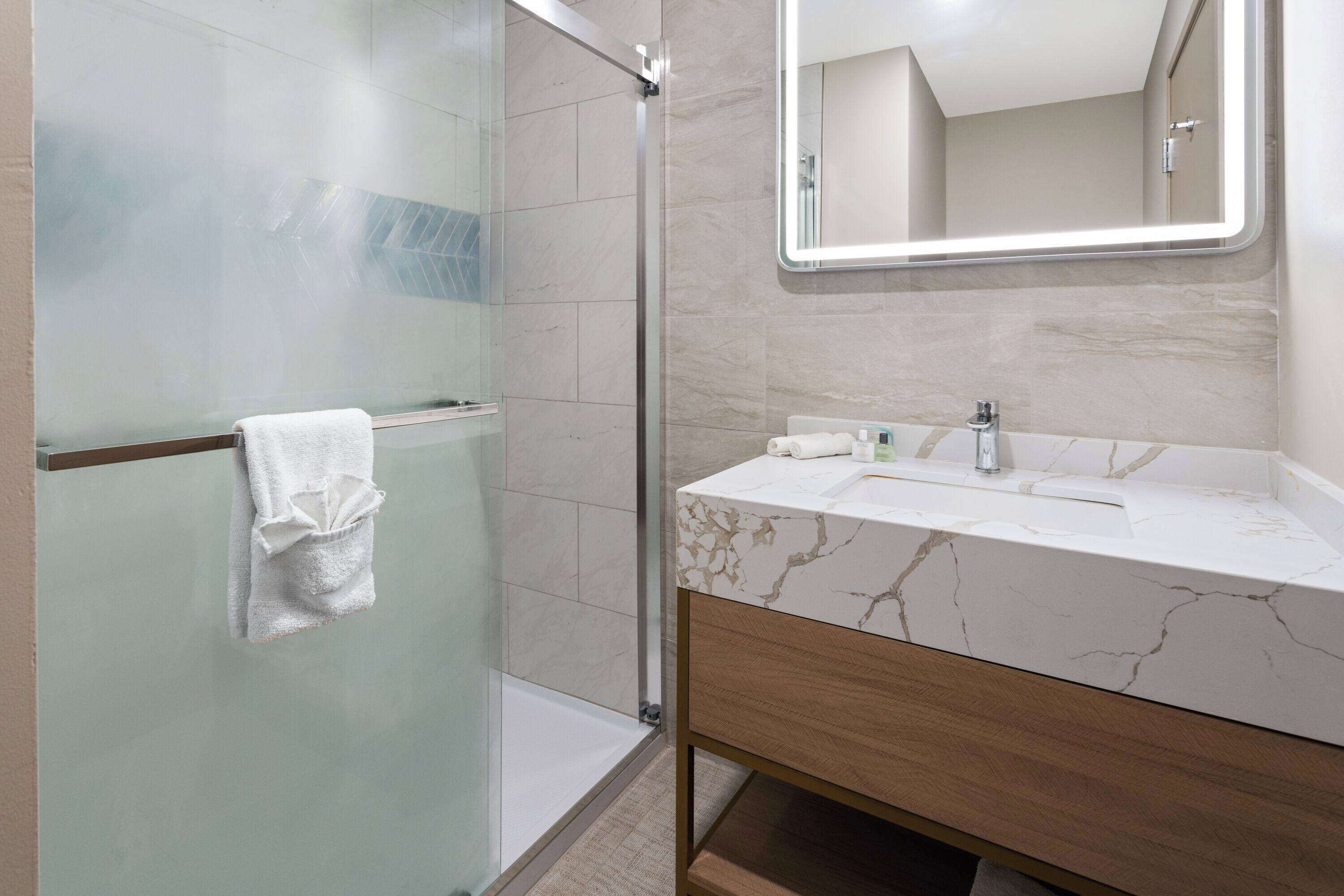 A modern bathroom with a glass-enclosed shower, a marble vanity, and a large mirror.