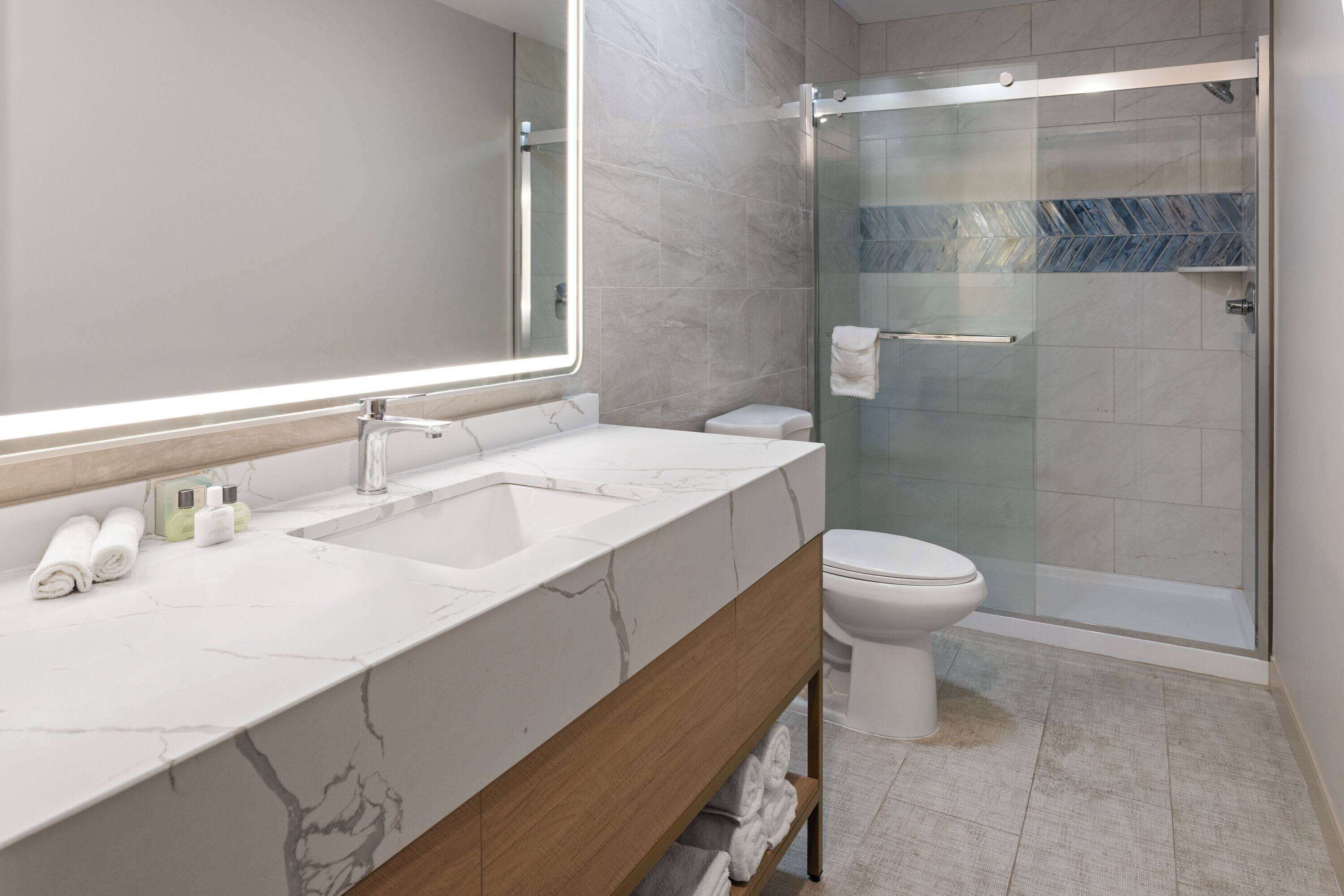 Un baño moderno con tocador de mármol, ducha con cerramiento de vidrio y un inodoro.
