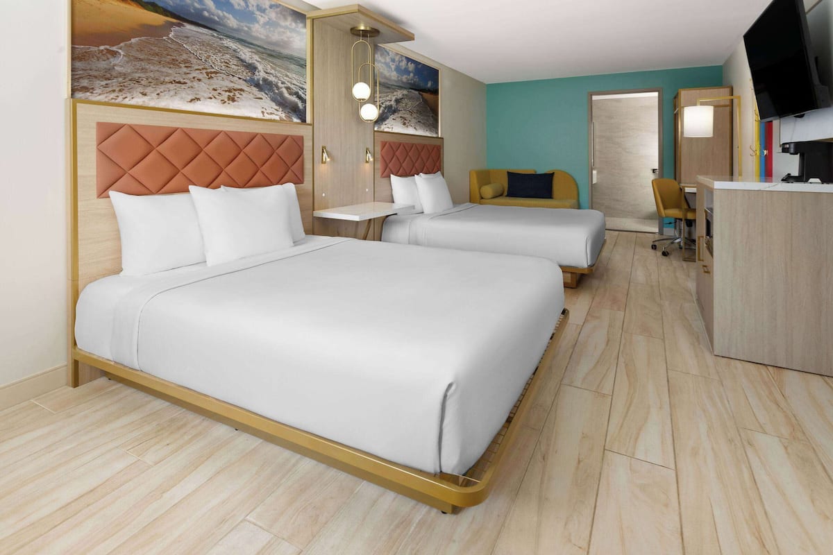 Una habitación de hotel con dos camas, un escritorio, una silla y un televisor.