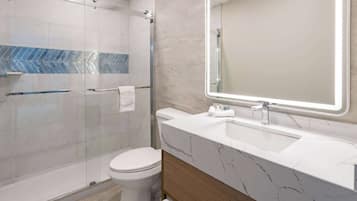 Une salle de bain moderne avec une douche à parois de verre, des toilettes, un lavabo en marbre et un grand miroir.
