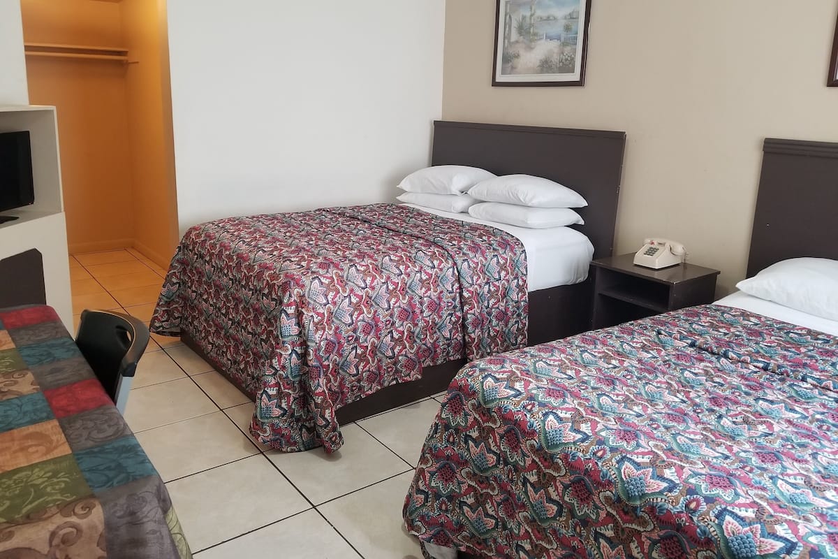 Une chambre d’hôtel avec deux lits, une télévision, un téléphone sur la table de chevet et un tableau au mur.