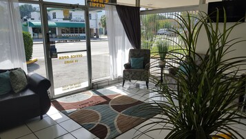 Un vestíbulo de hotel con una zona de estar, un amplio ventanal con vista a la calle y un letrero que anuncia un bar cercano.