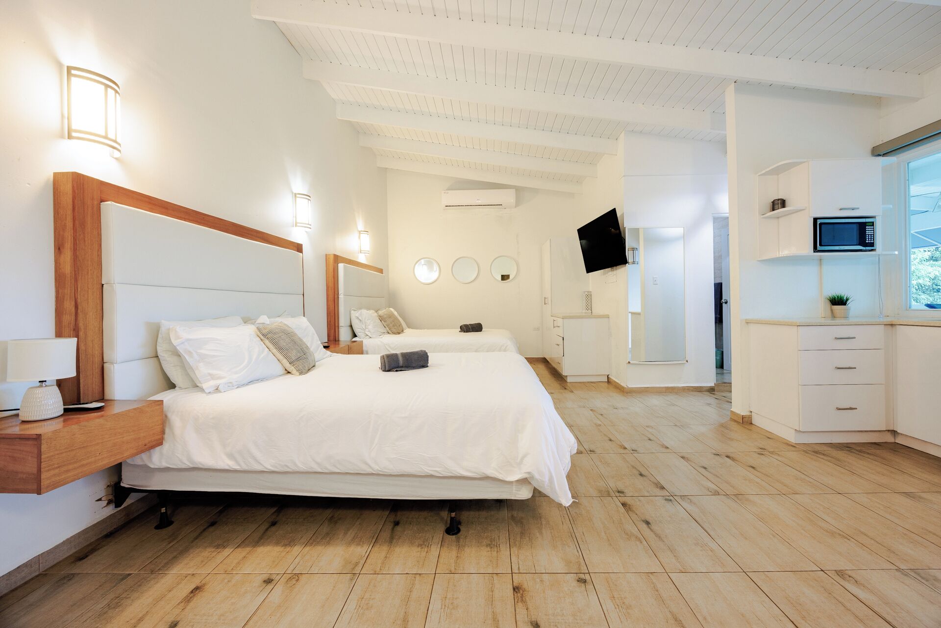 A modern hotel room with a large bed, a desk, a flat-screen TV, and a kitchenette.
