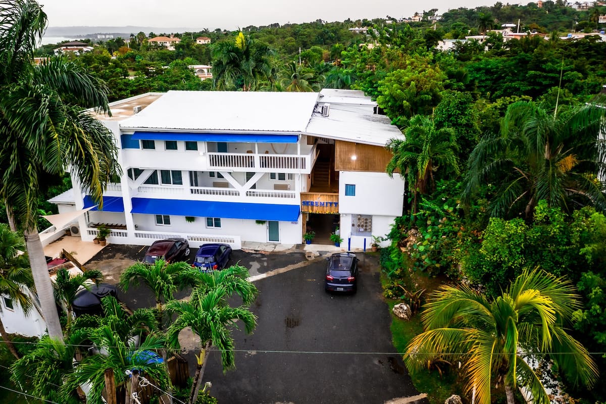A multi-story building with a blue and white facade, a covered outdoor area, and a parking lot.