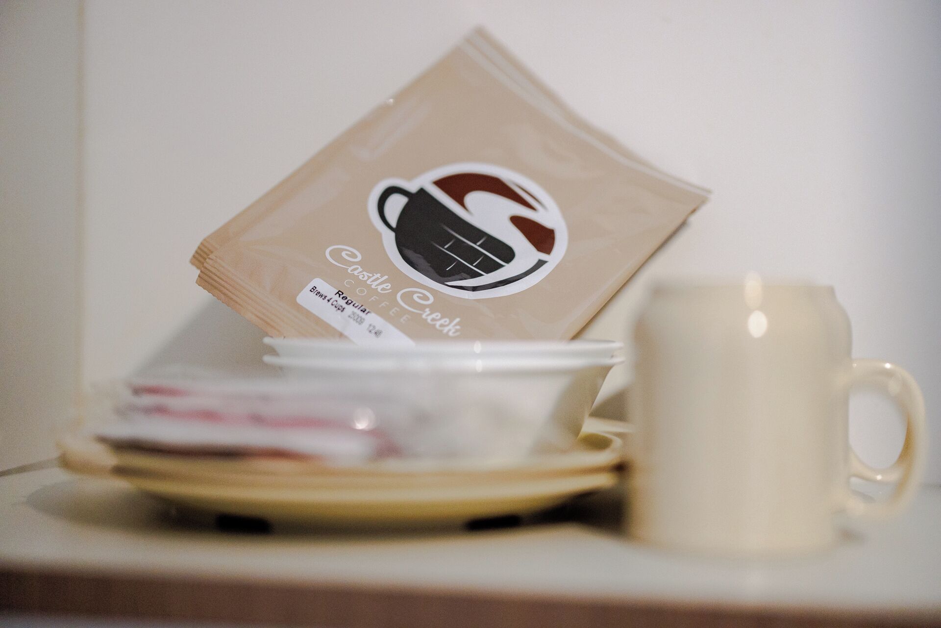 En kaffepose med teksten 'Castle Creek Coffee', samt en kop og underkop på et bord.