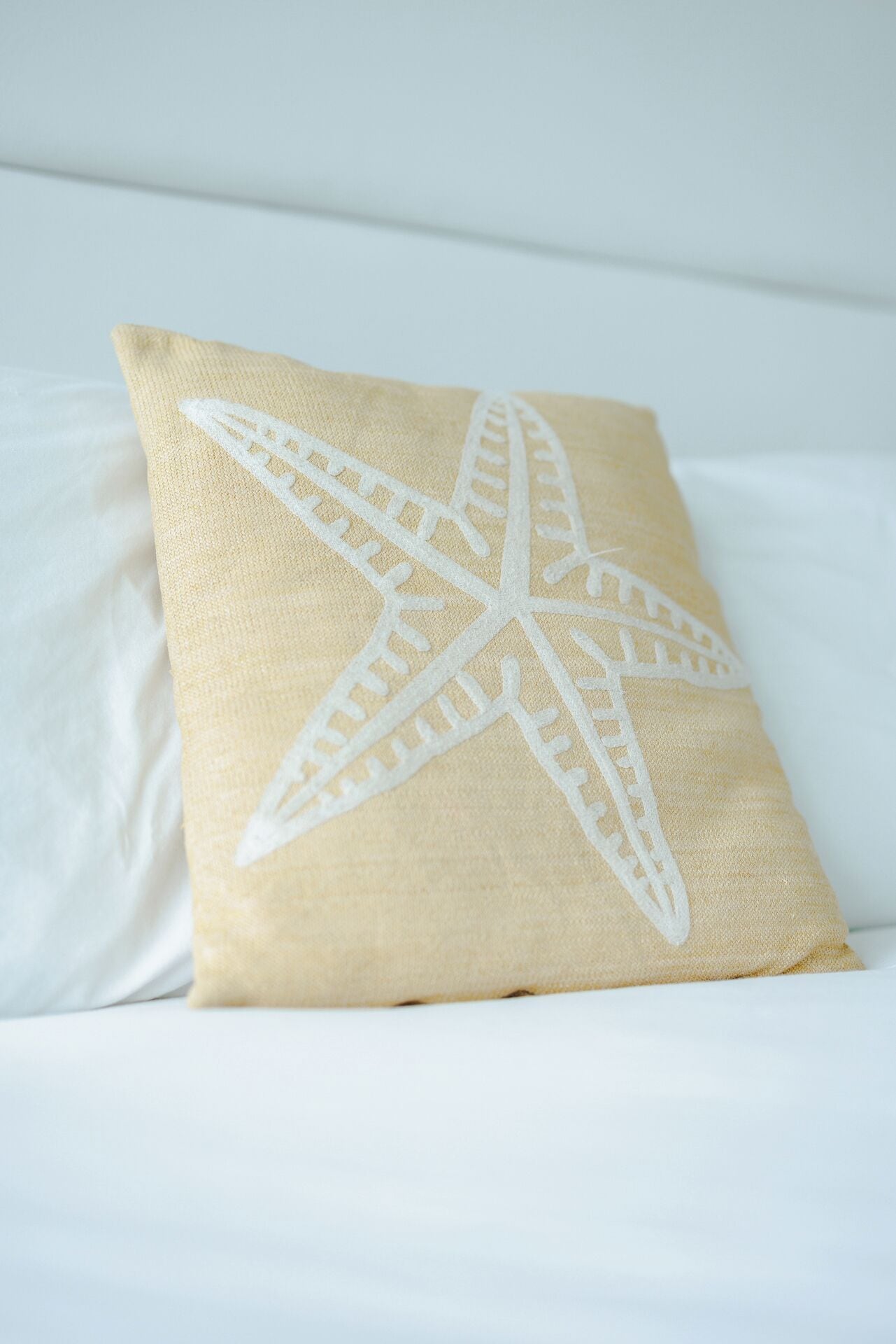 A pillow with a starfish design on a white bed.