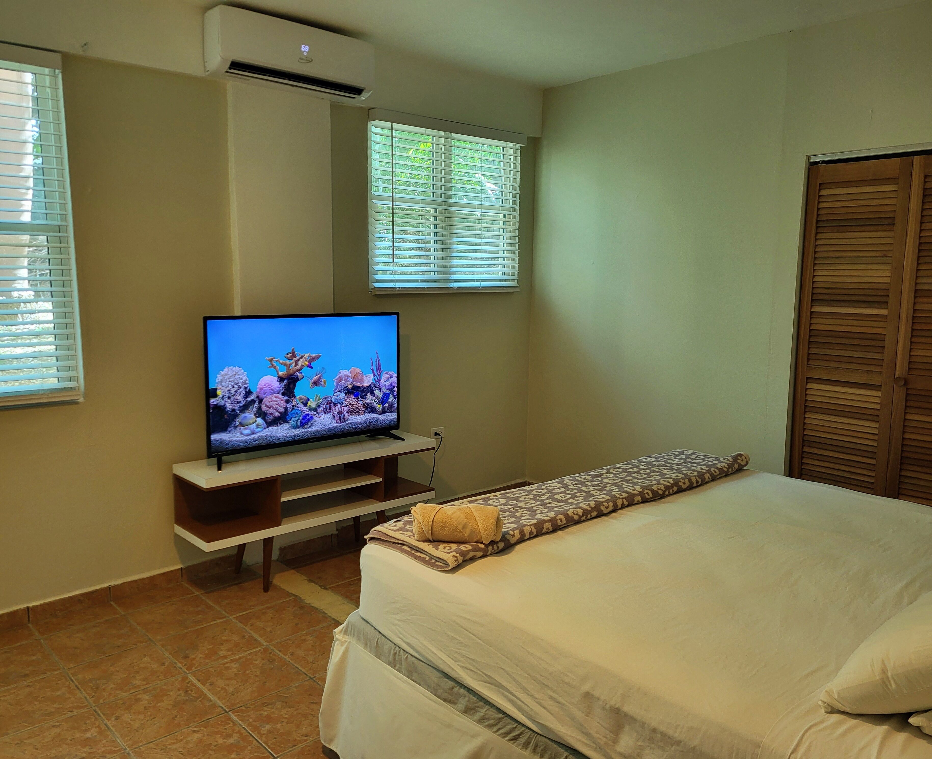 Ein Schlafzimmer mit einem Bett, einem Fernseher auf einem Schrank und einem Fenster mit Jalousien.
