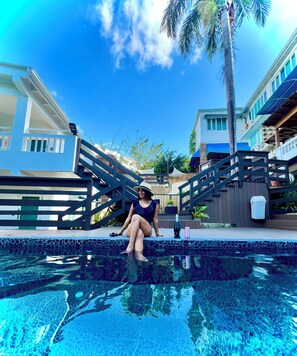 A person sitting by a swimming pool with a clear blue sky and palm trees in the background. - Serenity Rincon Guesthouse (Rincon)