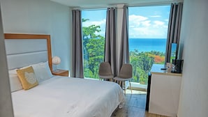A hotel room with a bed, a desk, two chairs, and a view of the ocean.