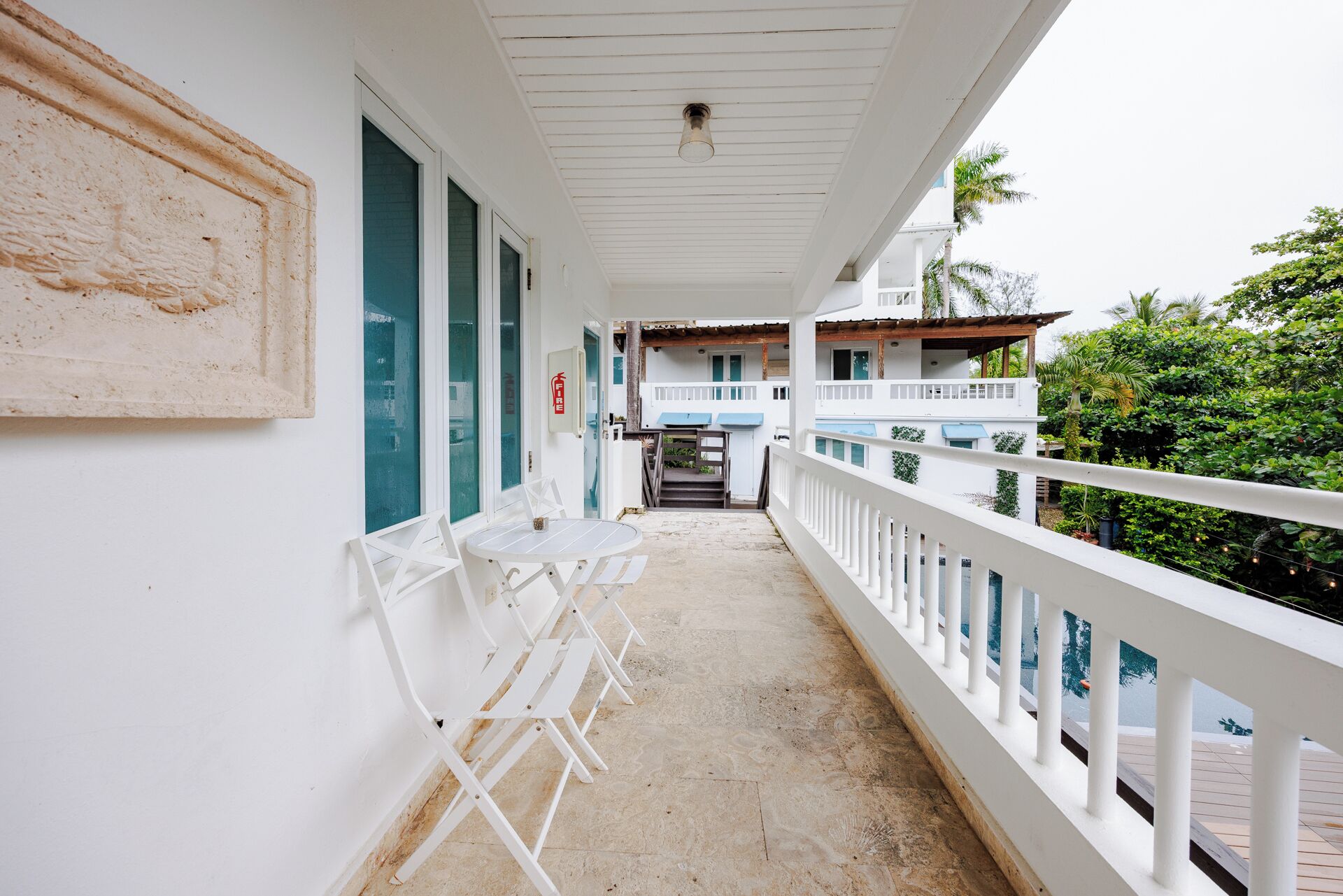 A covered balcony with white railings, a small table with chairs, and a view of a building with blue accents.
