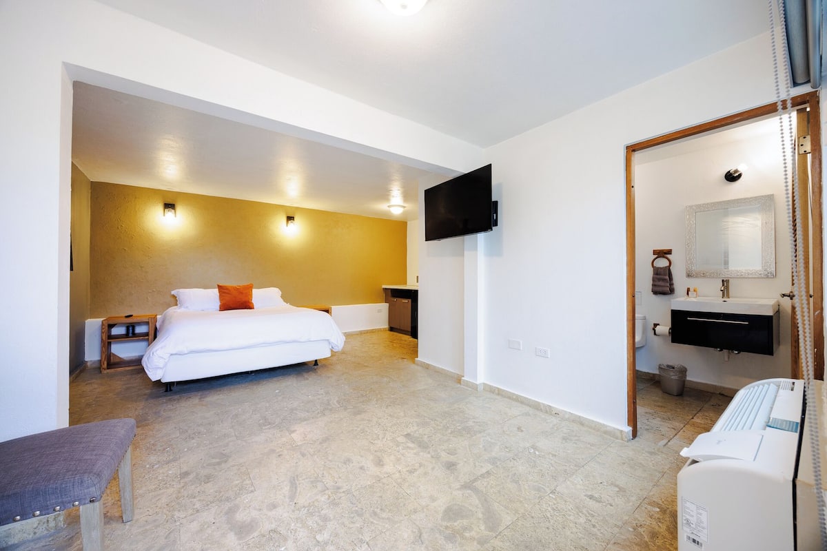 A hotel room with a bed, bedside table, TV, and a bathroom with a sink and mirror.