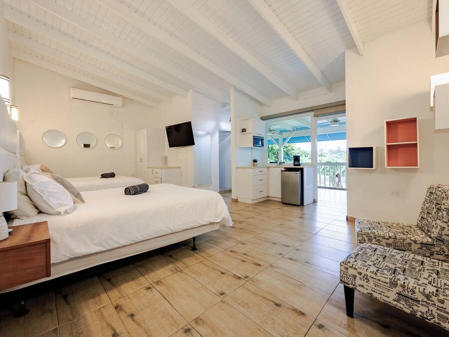 A hotel room with a large bed, a desk, a TV, a kitchenette, and a balcony with a view.