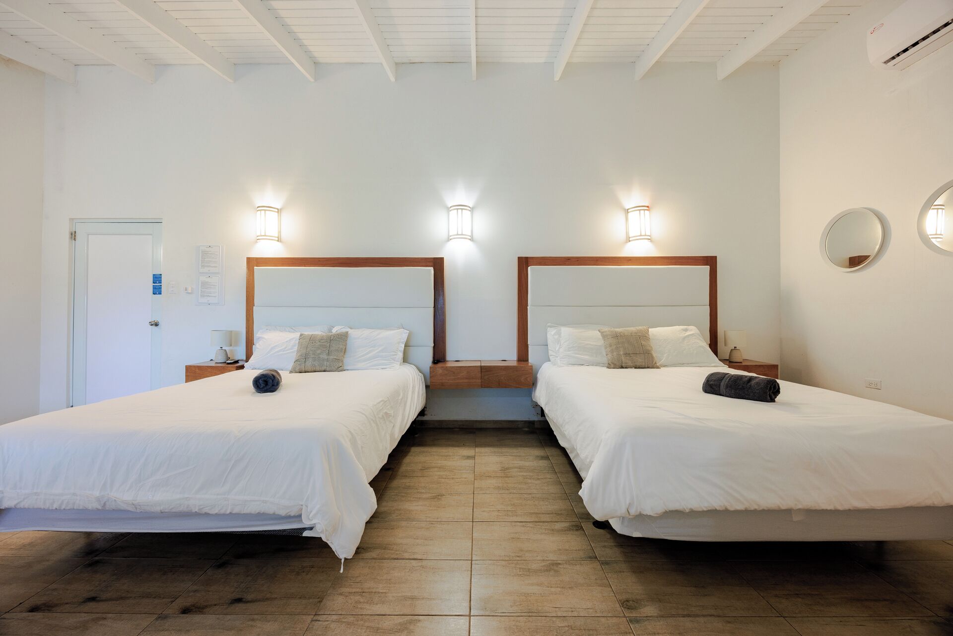 Habitación de hotel con dos camas, cabeceros de madera e iluminación de pared.