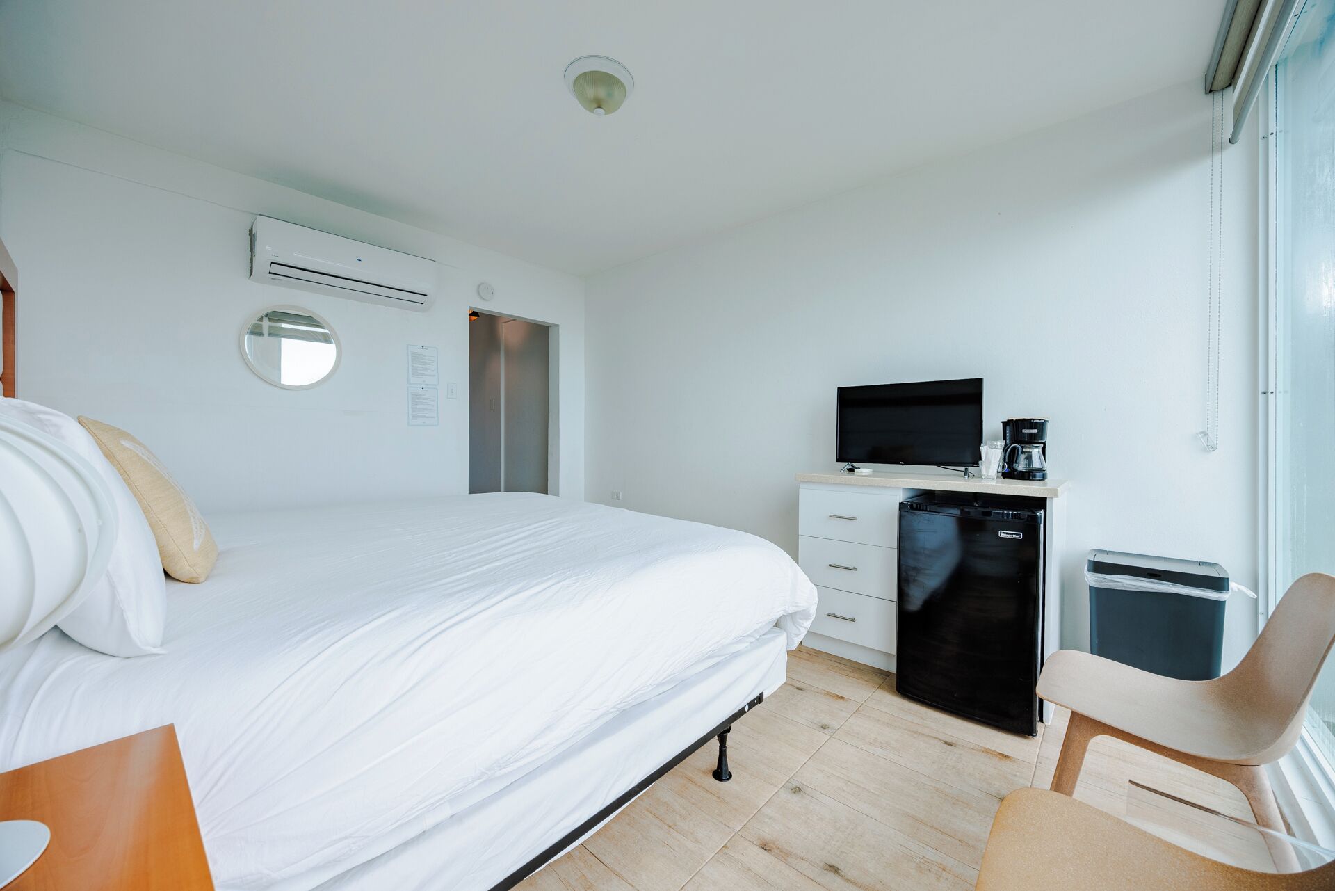 A hotel room with a bed, a desk with a television, a coffee maker, a refrigerator, and a chair.