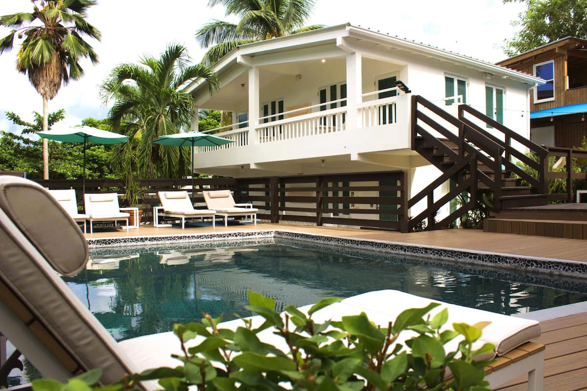 A two-story house with a pool, lounge chairs, and a wooden deck.
