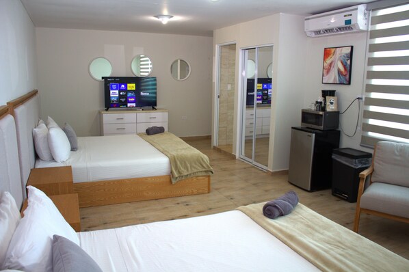 A hotel room with two beds, a TV, a microwave, and a small kitchenette.