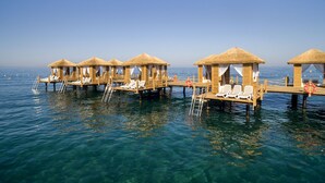 Des bungalows sur pilotis avec toits de chaume, des passerelles en bois et des chaises longues blanches.
