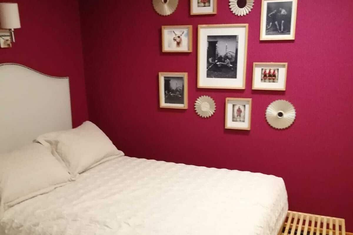 Un dormitorio con cama, cabecera, banco de madera y pared con marcos de cuadros.