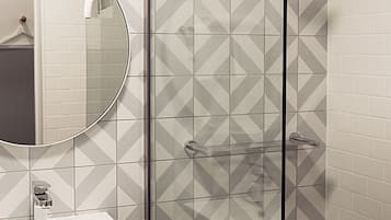 A bathroom with a glass shower enclosure, a white sink, and a mirror.