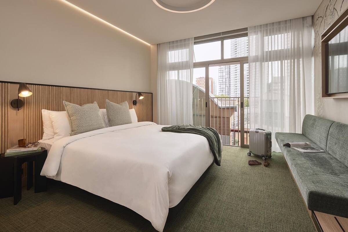 A hotel room with a bed, a sofa, a nightstand, a lamp, and a window with curtains.