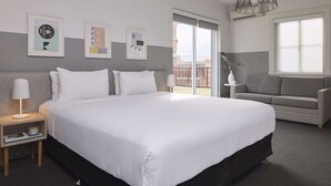 Una habitación de hotel moderna con una cama grande, un sofá, una mesita de noche y obras de arte en las paredes.