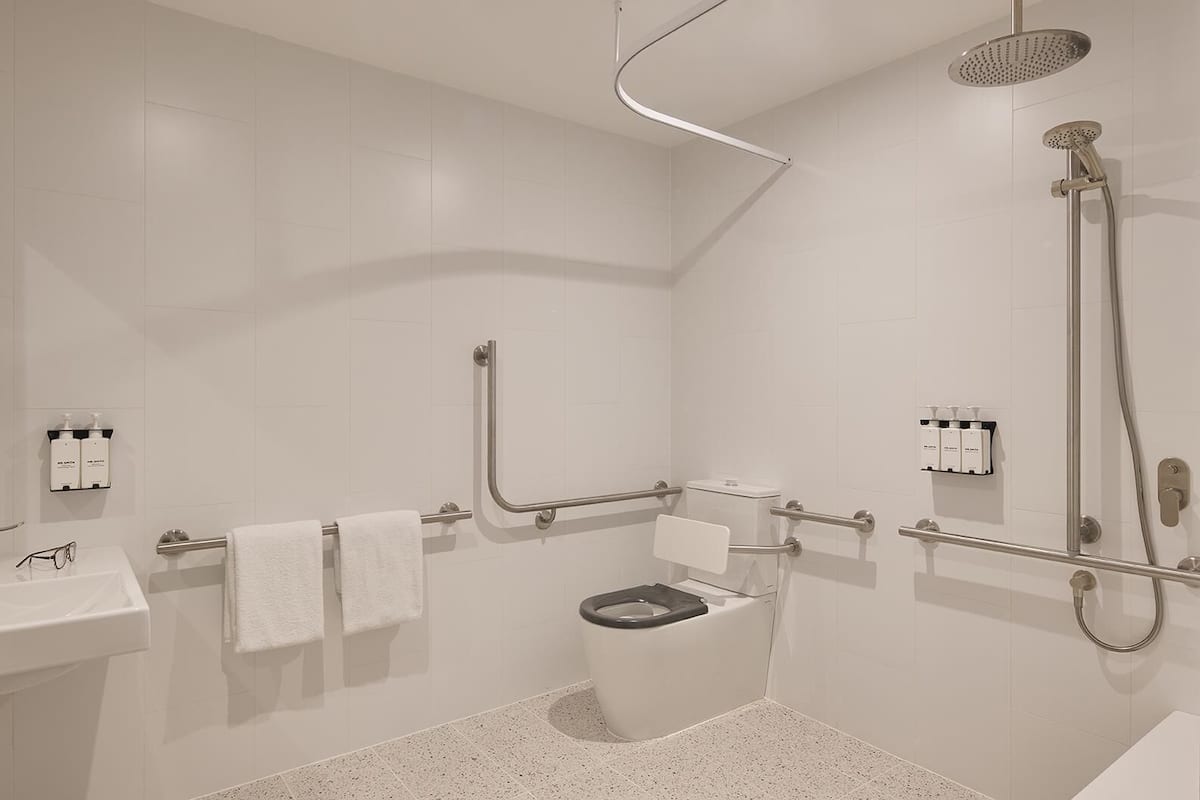 A modern bathroom with a shower, toilet, grab bars, and a sink with a towel rack.
