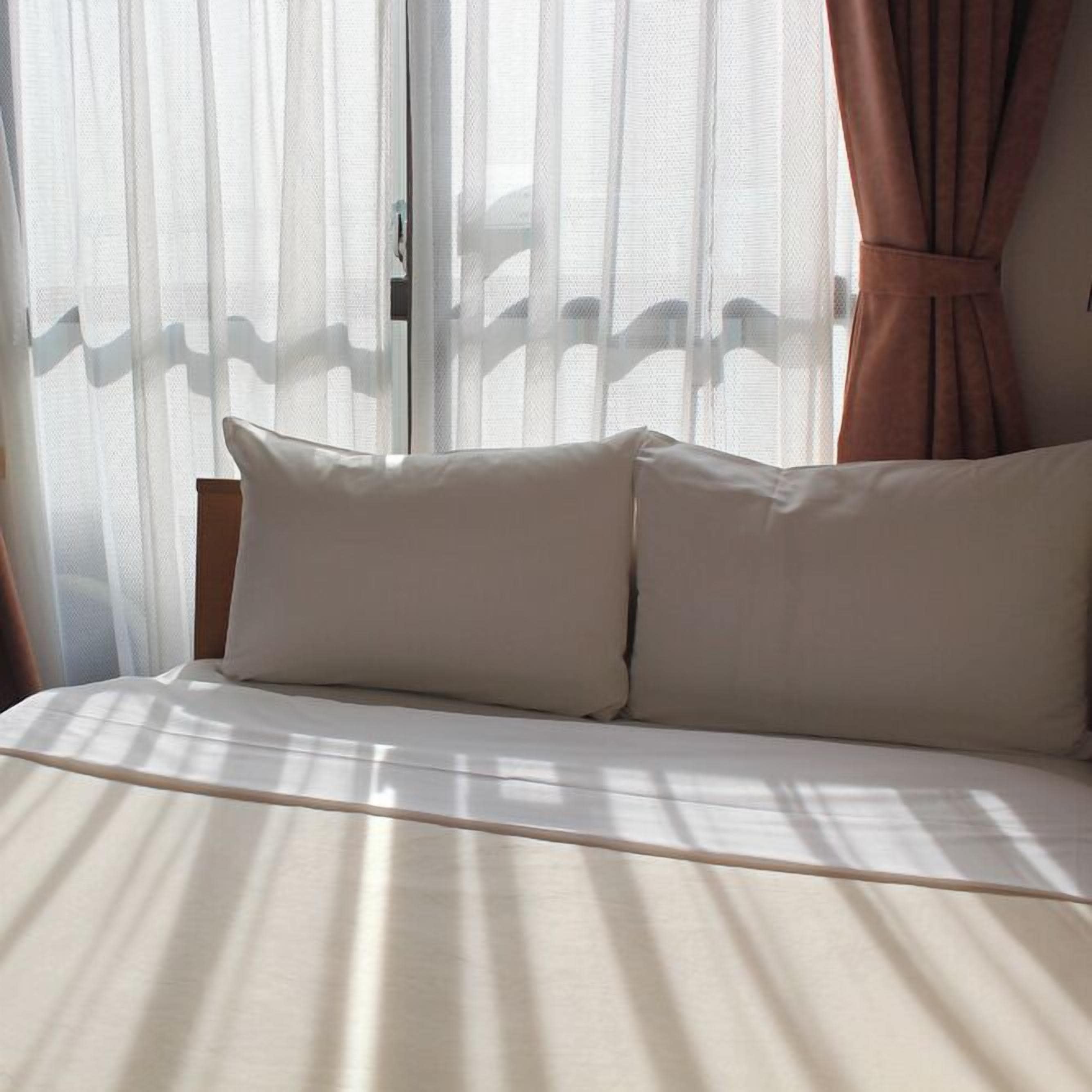 Una cama con ropa de cama blanca, cabecera de madera y cortinas de encaje.