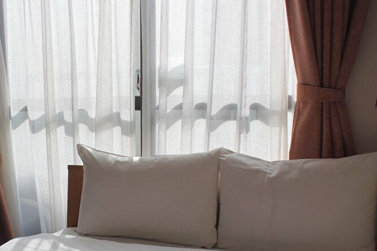 A bed with white bedding, a wooden headboard, and sheer curtains.