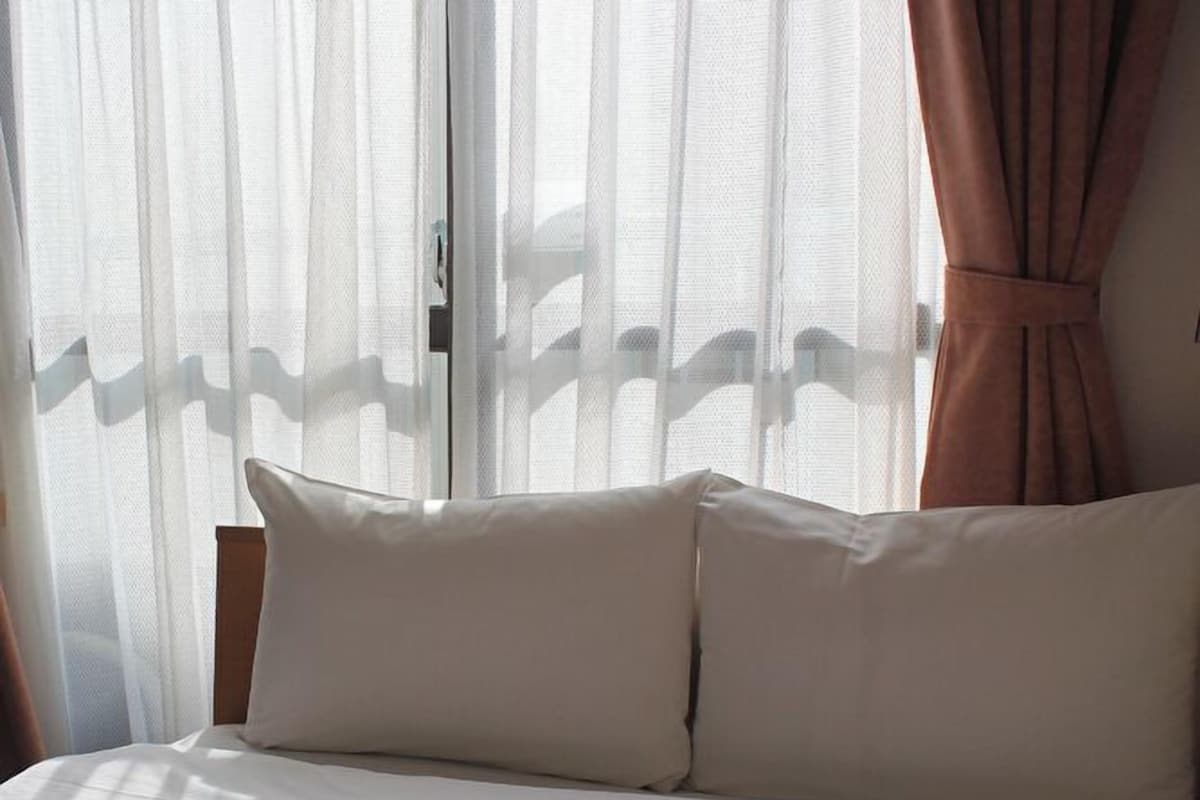 Una cama con ropa de cama blanca, cabecera de madera y cortinas de encaje.