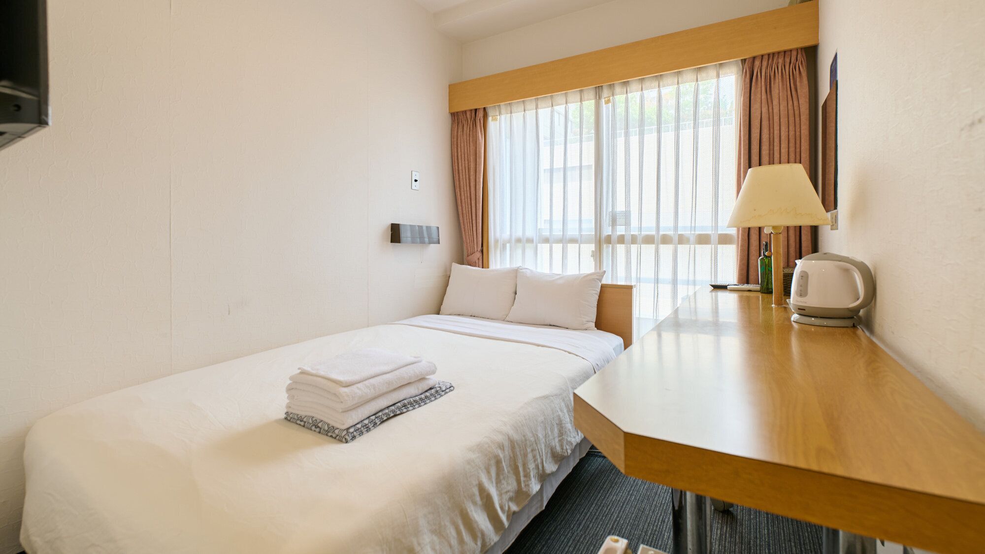 Een hotelkamer met een bed, een bureau, een lamp en een raam met gordijnen.