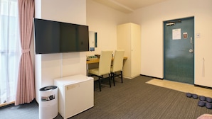 A hotel room with a flat-screen TV mounted on the wall, a small white refrigerator, a desk with a chair, and a door with a keycard reader. - Tabist Hotel Tetora Ikebukuro (Tokyo)