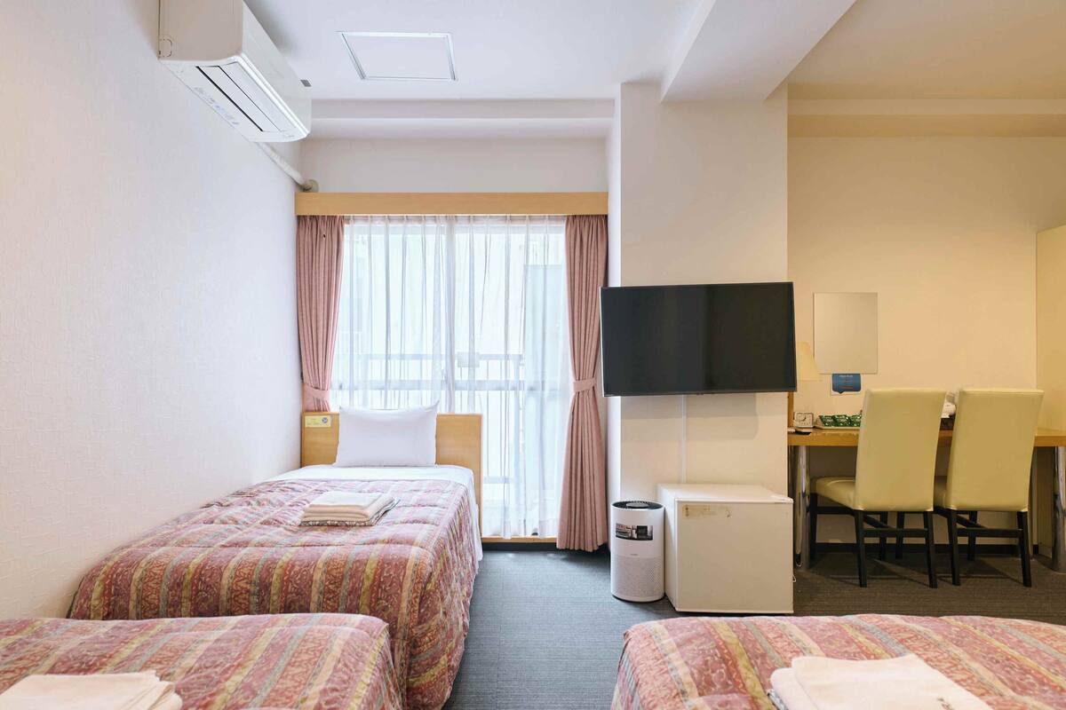 A hotel room with two beds, a desk, a television, and a waste bin.