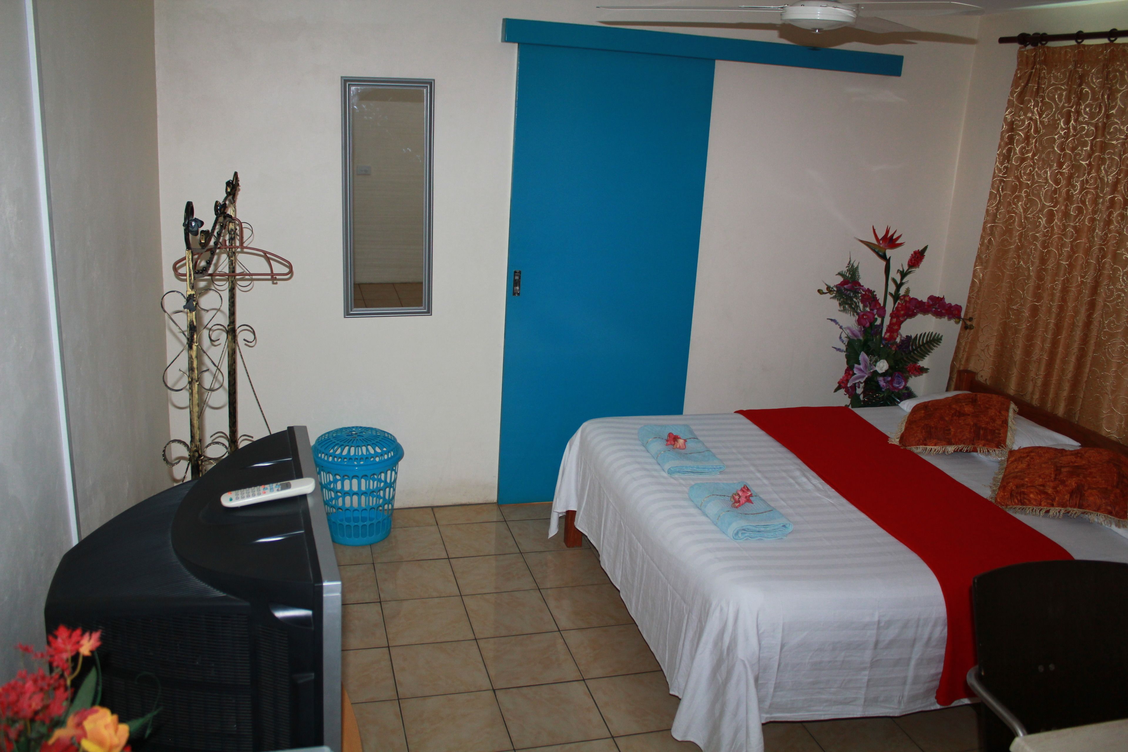 Habitación de hotel con cama, escritorio con televisor, puerta azul y ventana.
