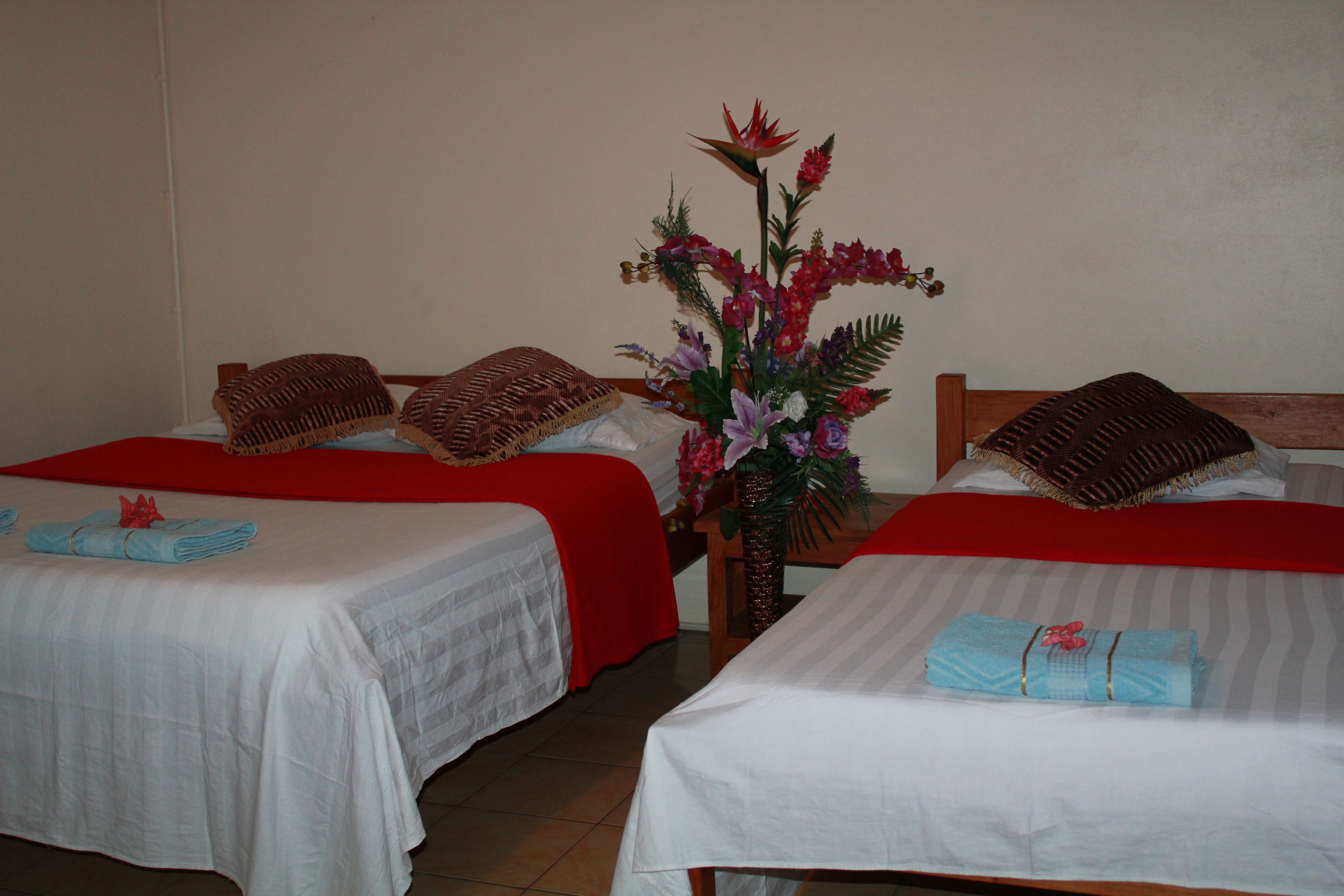Una habitación de hotel con dos camas, cada una con una colcha rojo y blanco, y una mesita con un florero de flores entre ellas.