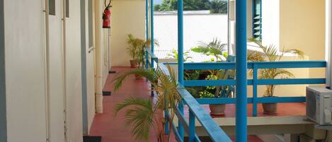 A covered corridor with red flooring, blue railings, and potted plants.
