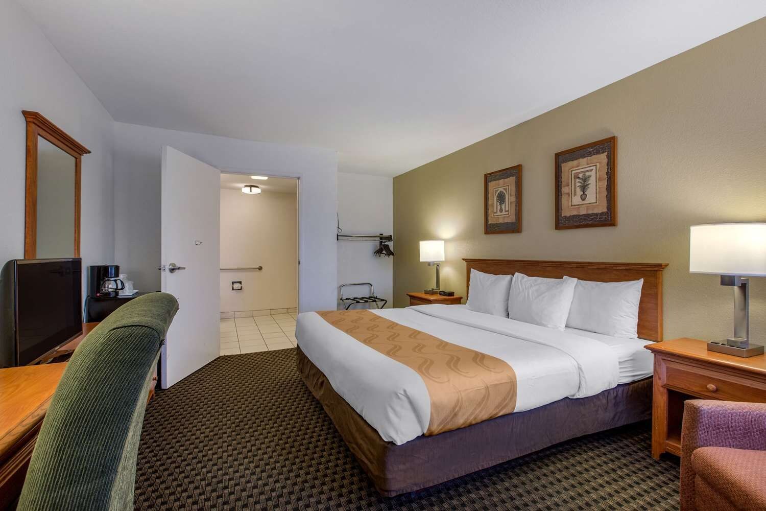 A hotel room with a bed, a desk, a chair, a television, and a bathroom door.